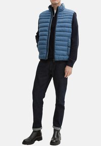 Lichtblauw gewatteerd vest met een ritssluiting, geribbeld kraag en horizontale stiksels. Gecombineerd met donkerdenim jeans en zwarte enkelboots.