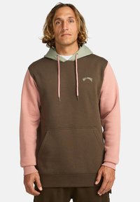 Sudadera bicolor marrón y rosa con capucha ajustable, bolsillo tipo canguro, puños acanalados y acento de logo en la parte superior del pecho. Textura de tela suave.