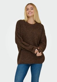 Brun strikket sweater med en afslappet pasform, rund halsudskæring og lange ærmer. Blød tekstur med ribbede manchetter og kantbånd. Båret over denim jeans.