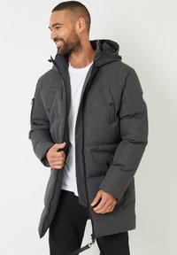Giacca parka grigia imbottita con cappuccio, cerniera frontale e molteplici tasche. Caratterizzata da una texture liscia e un design leggermente strutturato.