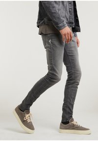 Jeans de mezclilla gris con un corte ajustado y un ligero desgaste, combinados con zapatillas de ante gris con suelas y cordones crema.