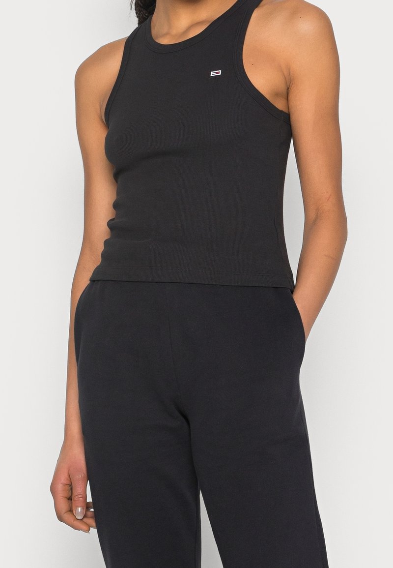 Svart ribbad linne med rundad halsringning. Har en liten broderad logotyp på bröstet. Materialet ser ut att vara stretchigt och figurnära.