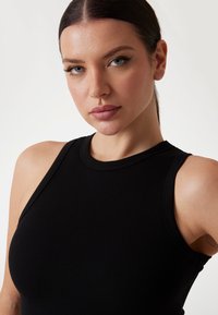 Sort ribbet tanktop med høj krave og uden ærmer; nærbillede der viser subtil tekstur og tætsiddende form.