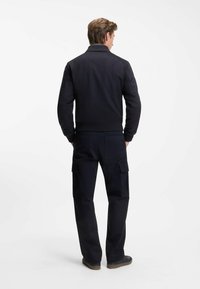 Navy blue sweater jacket with a fitted design, ribbed cuffs, and seam detailing, paired with dark cargo pants featuring multiple pockets.