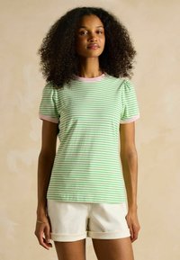 Green and white striped t-shirt with pink ribbed neckline and sleeves, short puff sleeves, paired with light-colored shorts.