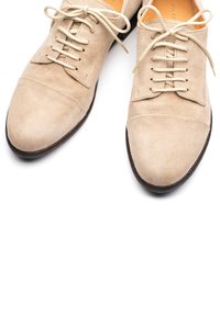 Scarpe in camoscio beige con punta arrotondata, dotate di sei occhielli e lacci beige. Texture liscia e suola in gomma scura. Design semplice.