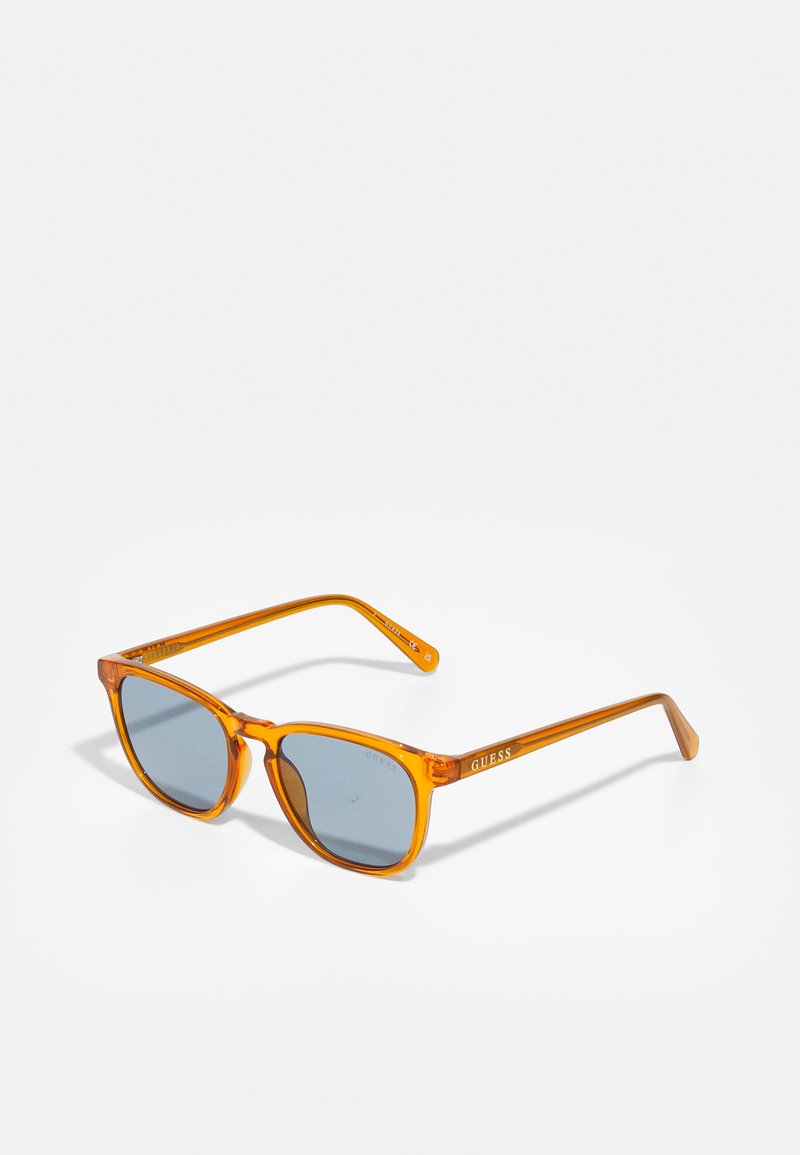 Orange akrylsolglasögon med grå linser, rektangulär design och varumärket "GUESS" tryckt på skalmen i vitt.