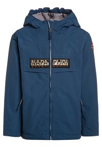 Chaqueta impermeable azul con capucha, cremallera frontal, dos bolsillos en el pecho y parches de logo. Presenta tejido texturizado y puños elásticos.