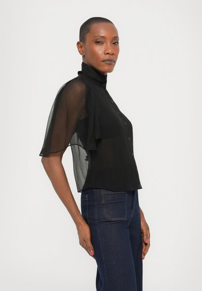 Black sheer short-sleeve blouse with a high collar, button-front design, and flowy fabric, paired with dark jeans.
