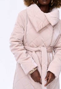 Lichtroze geborduurde jas met een grote kraag, een riem in de taille en lange mouwen, met een gladde, glanzende textuur en een ruitpatroon.