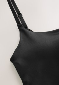 Soutien-gorge noir en tissu lisse et texturé. Comprend des bretelles réglables, un design sans coutures et un bord courbé pour une coupe ajustée.