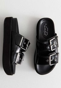 Černé platformové sandály s lesklým povrchem, vybavené dvěma nastavitelnými přezkami a tvarovanou stélkou pro pohodlí. Pevná gumová podešev.