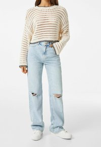 Ljuscremefärgad, öppet stickad tröja med svarta kanter, kombinerad med ljusblå, högmidjade jeans med slitna knän och vita sneakers.