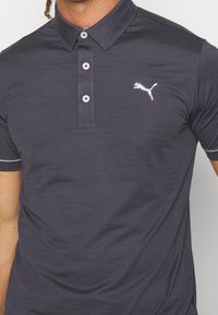 Námořnické polo tričko s jemnou texturou, s třemi knoflíky na klopě a bílým logem Puma na levé části hrudi. Obsahuje kontrastní šití na límci.