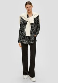 Zwart gemarmerd overhemdd blouse gecombineerd met zwarte trousers, een gedrapeerde witte sjaal en witte sneakers. Gladde stof, relaxte pasvorm.