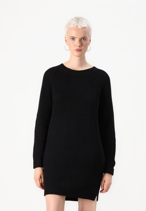 Vestido negro de punto con textura acanalada, cuello redondo y mangas largas. Aberturas laterales en el dobladillo. La tela parece gruesa y cálida.
