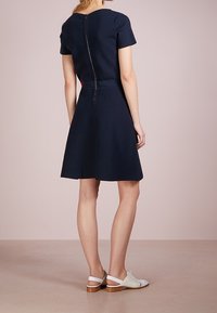 Marinblå klänning med kort ärm och en figursydd livdel samt en utsvängd kjol, med dragkedjestängning bak. Matchad med vita slip-on skor.