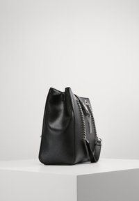 Sac fourre-tout en cuir noir avec texture, accents en chaîne argentée et forme structurée. Il possède une seule bandoulière et une fermeture éclair.