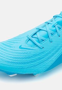Lystblå atletiske sko med struktureret syntetisk overdel, der har kryds-lace struktur, strømlinet design og hvide dæmpestifter på sålen.