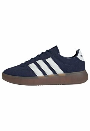 Granatowy sneaker Adidas z białymi trzema paskami po boku i półprzezroczystą brązową podeszwą, widziany od zewnętrznej strony.
