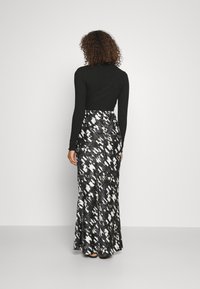 Haut à manches longues noir côtelé associé à une jupe maxi avec un motif abstrait noir, blanc et gris, texture lisse et taille ajustée.