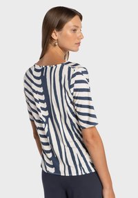 Granatowo-biały top w paski z krótkim rękawem, miękki, lekki materiał, okrągły dekolt, posiada nieregularny wzór.