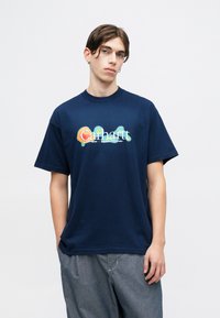 T-shirt in cotone blu navy con un grande logo "Carhartt" colorato in un font moderno sul petto, maniche corte e vestibilità comoda.