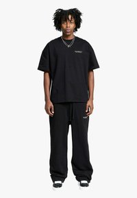 T-shirt nera a maniche corte con vestibilità comoda e joggers abbondanti coordinati, entrambi con marchio minimo. Il tessuto sembra morbido con una texture liscia.