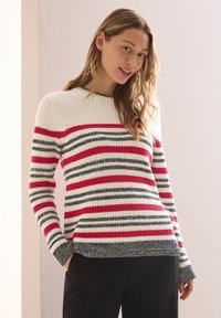 Randig tröja i off-white, röd och grå. Stickad textur med långa ärmar, rund halsringning och ribbad nederkant. Bärs med svarta byxor.