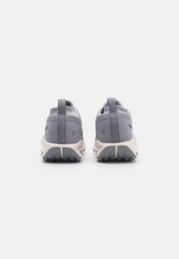 Scarpe sportive grigie con tomaia in mesh testurizzato, suola beige a contrasto e accenti riflettenti. Presentano un'etichetta di trazione sul tallone.