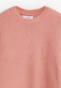 Suéter rosa claro hecho de tela de punto suave y esponjosa con cuello redondo y puños acanalados, presentado con sutiles variaciones de textura.