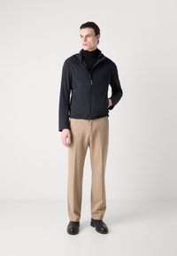 Black, zip-up jacket with a hood, made of smooth, lightweight material. Paired with beige trousers and black shoes. Minimalistic design.