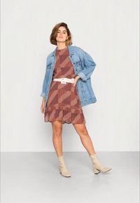 Casaco de ganga sobre um vestido castanho com padrão e rendas. Cinto branco, botins crème. Texturas suaves, padrões geométricos e com pintas.