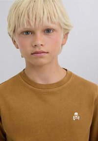 Brown long-sleeve shirt with a rounded neckline. Features a white skull and crossbones design on the left chest. Soft, smooth texture.