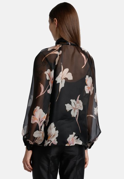 Blusa nera floreale in tessuto trasparente, con grandi motivi floreali bianchi e rosa, maniche a palloncino e orlo arrotondato. Texture liscia.