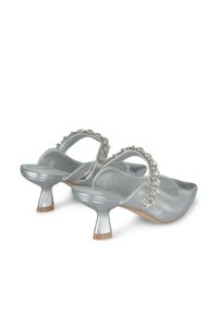 Scarpe con tacco in metallo argento, con punta quadrata, cinturino decorativo con cristalli e tacco corto a campana. Texture liscia.