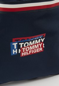 Tela azul marino con logotipos de Tommy Hilfiger en capas en rojo, blanco y azul, y un ribete a rayas en rojo, blanco y azul marino en la parte superior.