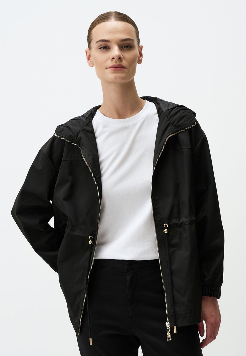 Zwarte hoodiejas met een ritssluiting aan de voorkant, elastische manchetten en een trekkoord in de taille. De stof lijkt glad en lichtgewicht. Eenvoudig ontwerp.