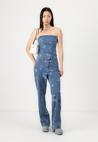 Denim stroppeløs topp og flagrende jeans med kirsebærmønster. Lys blått stoff, glatt tekstur og subtile hardware-detaljer.