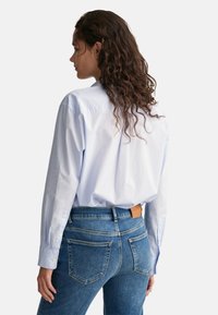 Light blue button-up shirt with long sleeves, paired with faded blue jeans featuring a leather patch and classic back pocket design.