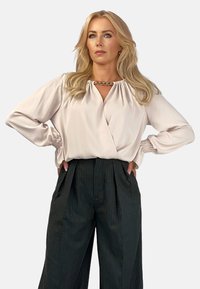 Jasnoróżowa satynowa bluzka z dekoltem w serek i marszczonym kołnierzykiem, w połączeniu z czarnymi spodniami w prążki z wysokim stanem, ozdobionymi plisowanym przodem i szerokimi nogawkami.