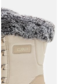 Botte d'hiver beige avec bordure en fausse fourrure grise, tige en tissu texturé et ferrures métalliques pour les lacets. Logo CMP sur une étiquette rectangulaire.