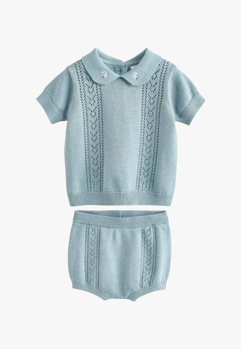 Jasnoniebieski dzianinowy zestaw składający się z krótkiego topu z kołnierzykiem i wzorzystymi detalami, w połączeniu z dopasowanymi szortami.