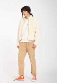 Creme fleecejakke med ståkrave, lynlås lomme, beige corduroy bukser og orange høj-top sneakers. Simpelt design og teksturerede materialer.