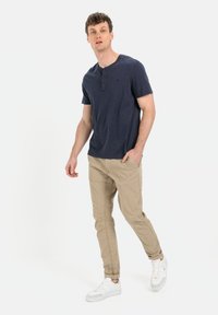 Granatowa koszulka henley z krótkim rękawem, z trzema guzikami, w połączeniu z beżowymi chinosami o slim fit i białymi sneakersami. Casualowy strój, prosty design.