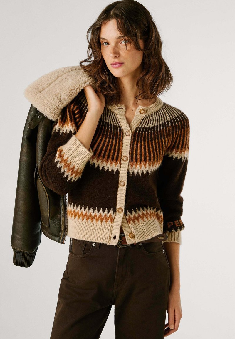 Cardigan en tricot marron avec des motifs en zigzag crème et rouille, doté d'une fermeture à boutons et de poignets côtelés, associé à une veste bombardier verte.