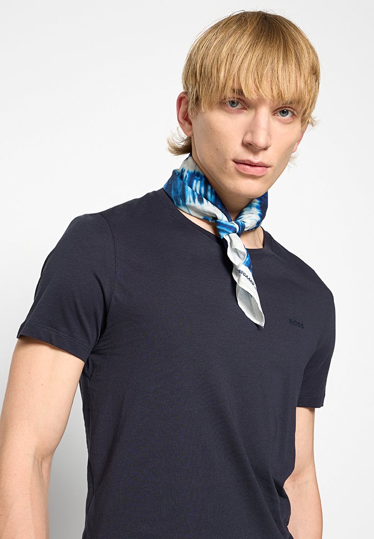 Seidenschal mit blau-weißem Batikmuster um den Hals einer Person, die ein dunkel gefärbtes T-Shirt trägt. Glatte Textur, lässiges Design.