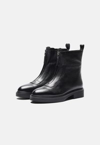 Botas de tobillo de cuero negro con cierre de cremallera, punta redondeada, acabado texturizado y un tacón bajo cuadrado. Disponen de tiradores para facilitar su uso.