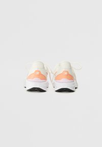 Zapatillas deportivas blancas y durazno con un upper texturizado, punta redonda y cordones blancos. Presentan un acento curvado en el talón trasero y una suela de goma.