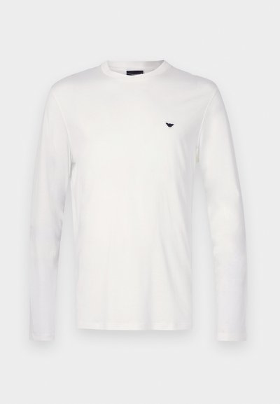 Fehér, hosszú ujjú pamut póló kerek nyakkal. A mellkason egy kis sötétkék logó látható. Simább textúrájú és normál szabású.